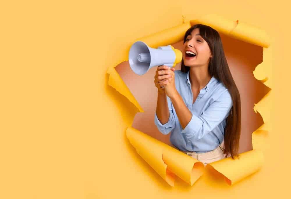 Pessoa anunciando através de megafone o lançamento de uma campanha de marketing digital pela agência de marketing. Aprenda conosco como vender mais no inicio do ano.