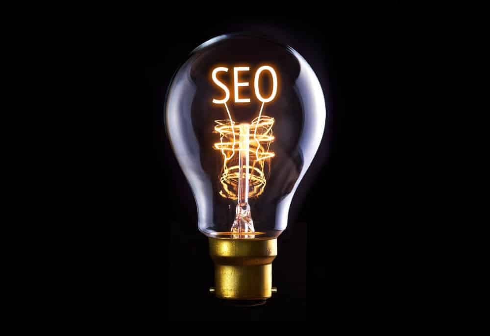 Lâmpada acesa com a palavra 'SEO' destacada, simbolizando o lançamento de estratégias de marketing digital por uma agência de marketing especializada em SEO e criação de sites.