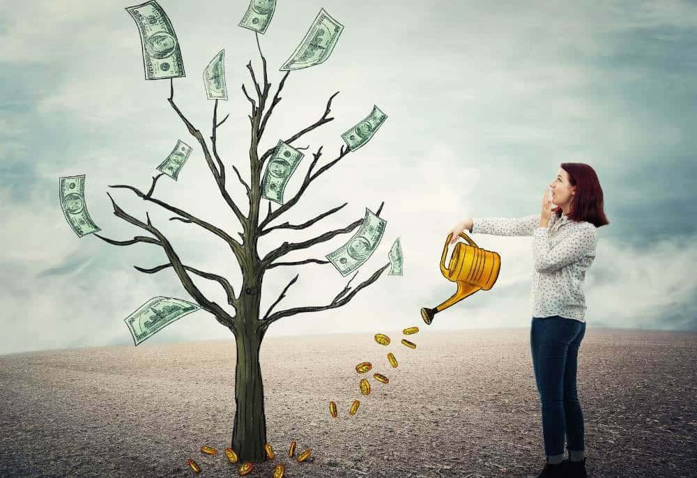 Mulher regando uma árvore seca com um regador amarelo ilustrado, de onde caem moedas. A árvore tem cédulas de dinheiro nos galhos, simbolizando investimento e crescimento financeiro. Imagem conceitual sobre "Renda Extra"