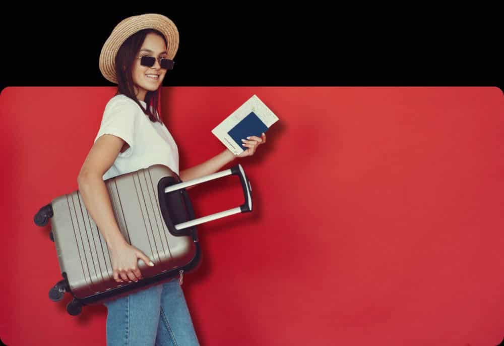 Uma mulher vestindo uma camiseta branca e jeans, segurando uma mala de viagem prateada e um passaporte azul, pronta para uma nova aventura. Estratégias para viajar.